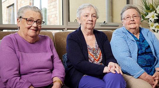 three elderly sisters sitting on a couch together in an aged care home