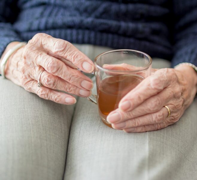 An elderly person's hand holding a glass of tea in her lap