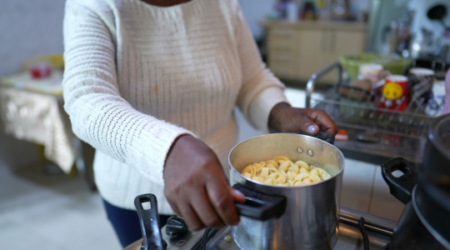 close up of black lady placing large pot of pasta on stove top