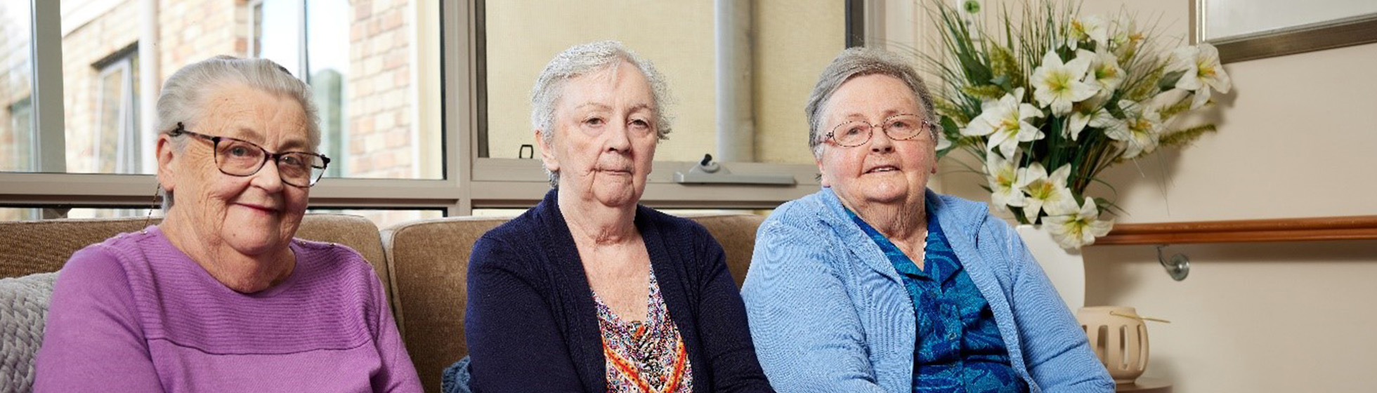 three elderly sisters sitting on a couch together in an aged care home
