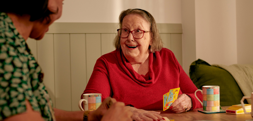 Older lady with red jumper smiling whilst playing cards