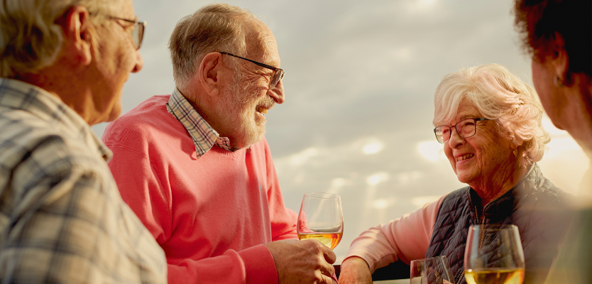 Four residents in retirement apartment drink white wine smiling