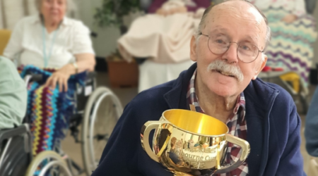 Elderly male resident smiles at the camera at Calvary St Joseph's aged care home holding the melbourne cup